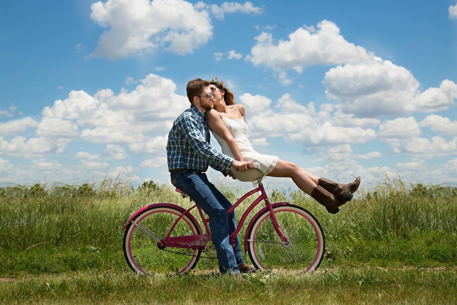 A man and woman kissing on top of a bicycle.